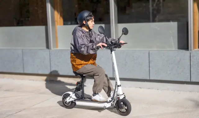 ヘルメットをかぶった人が座り乗り電動キックボードに乗っている