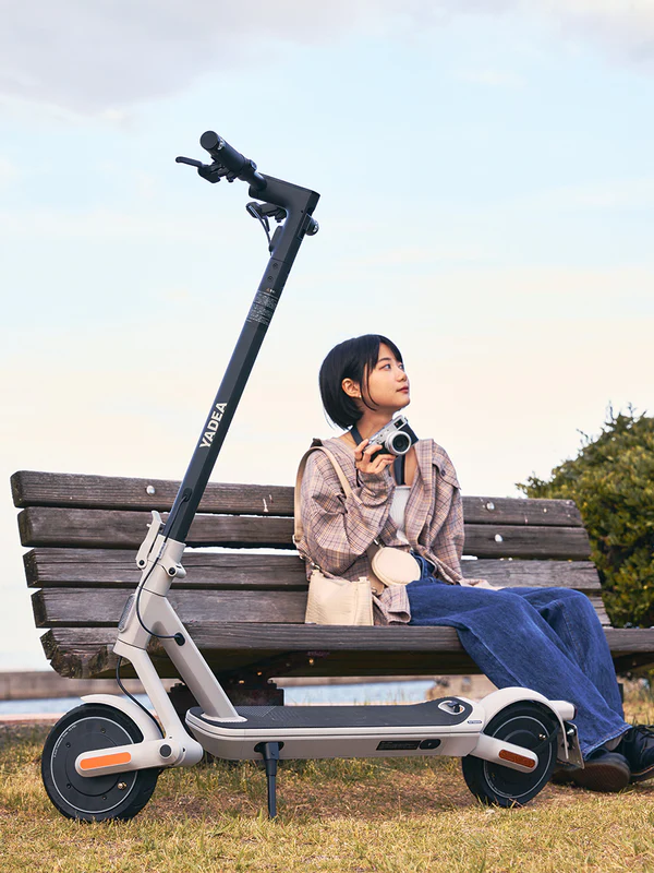 ベンチに座ってカメラを持つ女性と電動キックスクーター