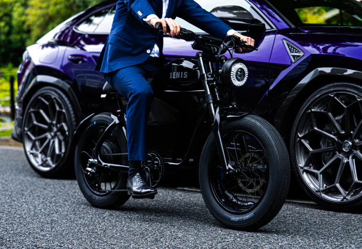 スーツ姿の男性が紫色の車の前で電動バイクに乗っている写真