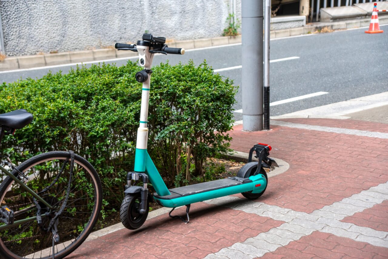 歩道の植え込みと自転車の隣に駐輪された、エメラルドグリーンと白のシェアリング用電動キックボード